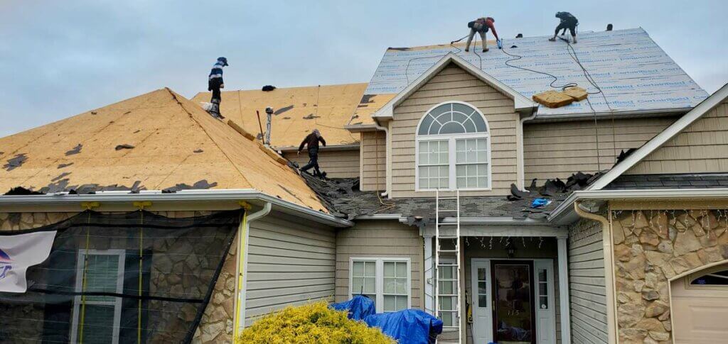 Team of professional roofers, working with top roofing companies in Winston-Salem, install a two-story home's roof.